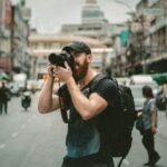 A man in the middle of street taking a photo with his camera