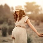 A pregnant lady holding his partners hand in golden hour