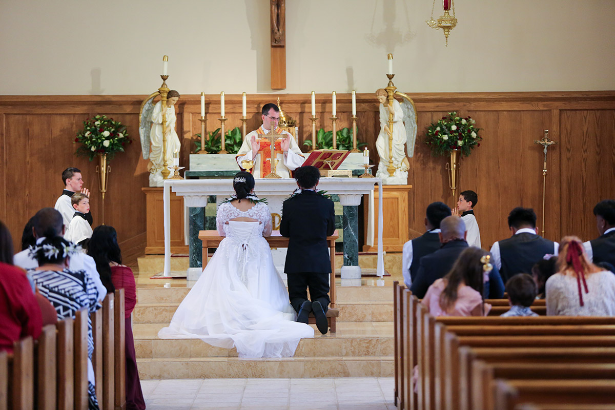A photo of a couple kneeling before the preist in the church.