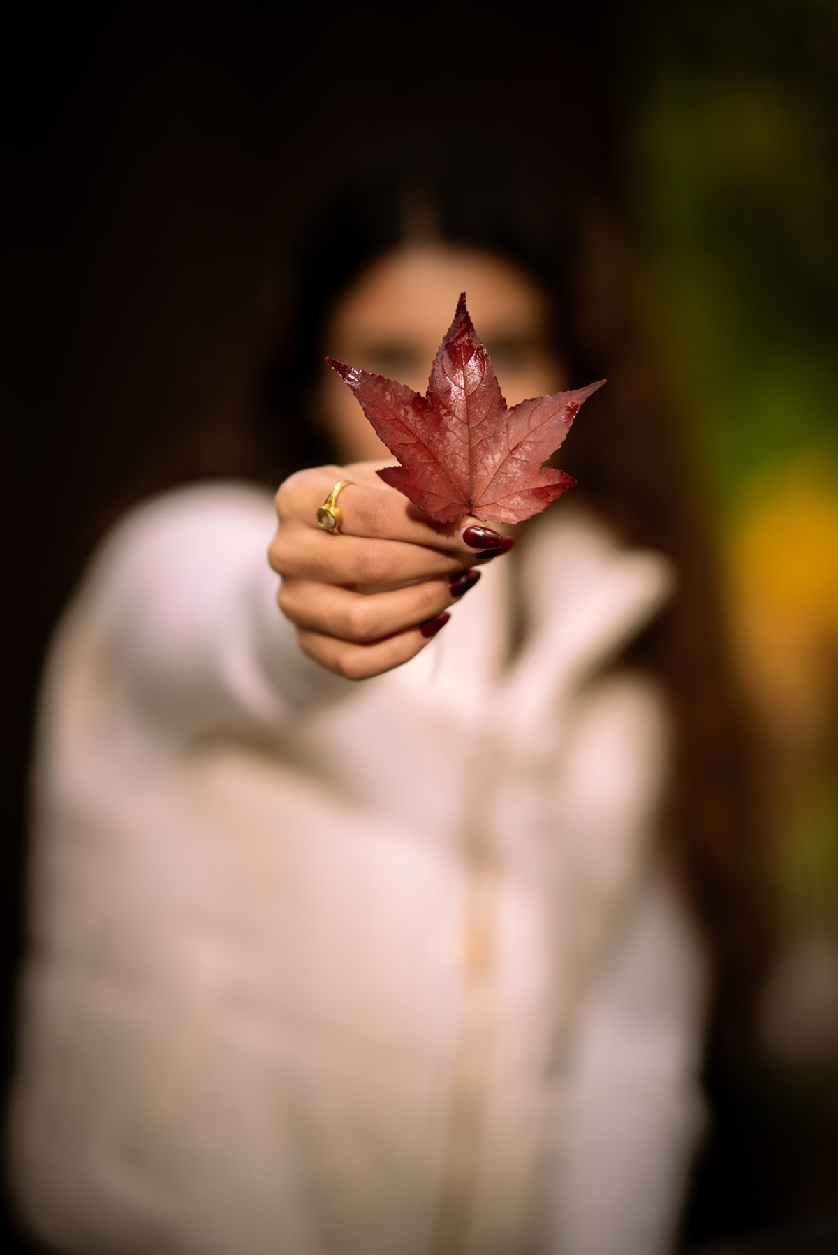A woman portrait photo holding a leaf in front of her face.